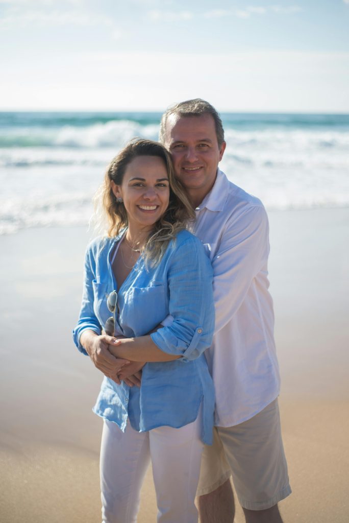 miling couple embracing on the beach with ocean waves in the background on a sunny day.
